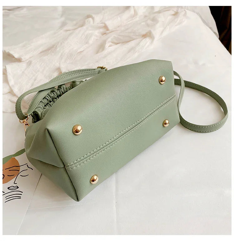 sage green leather crossbody bag with gold studs and adjustable strap on white fabric