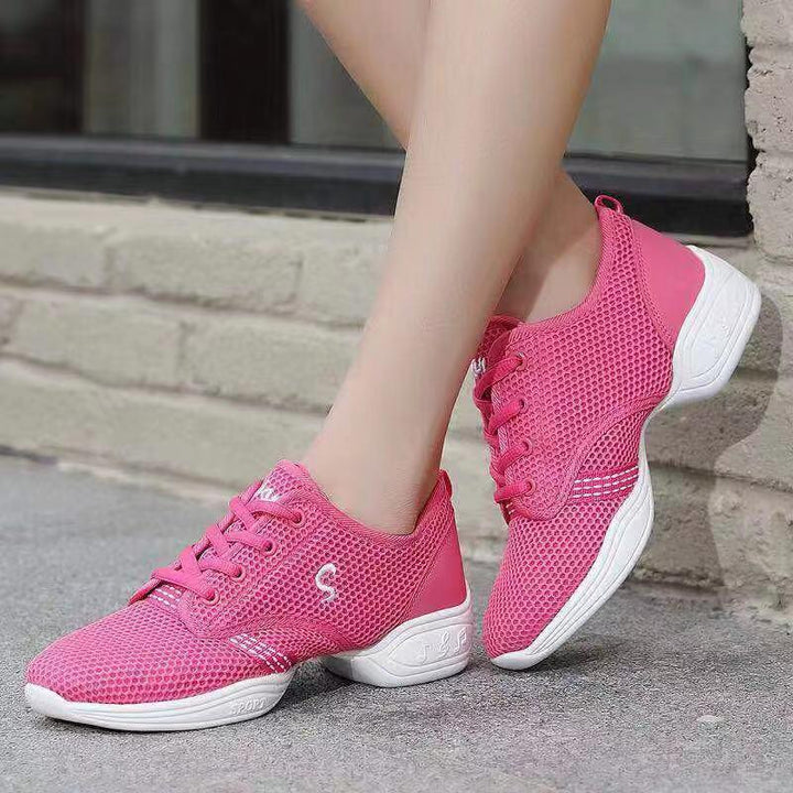 Pair of bright pink breathable mesh dance sneakers with white soles worn outdoors