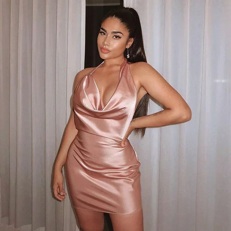 woman wearing a pink satin halter neck mini dress posing indoors with one hand on hip