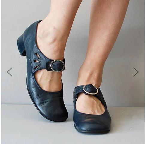 Black leather Mary Jane shoes with round buckle and cutout details worn on feet