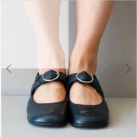 Pair of black Mary Jane shoes with buckles worn on feet of different skin tones against neutral background