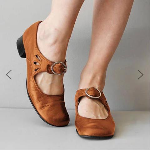 Brown leather Mary Jane shoes with round buckles on feet against a plain background