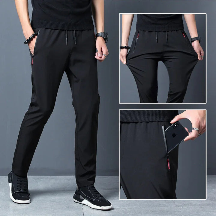 Men's black casual stretch jogger pants with zipper pockets, elastic waistband, and drawstring, worn with black sneakers