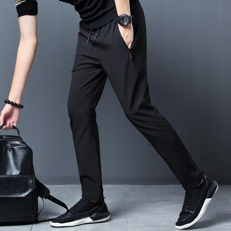 Man wearing black jogger pants, black sneakers, and black watch, carrying black leather backpack