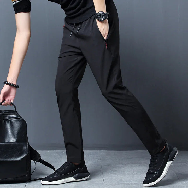 Man wearing black jogger pants, black sneakers, and black watch, carrying black leather backpack