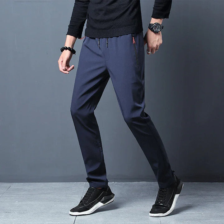 Man wearing navy blue casual pants and black sneakers against grey background
