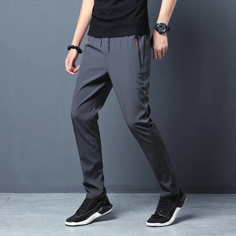 Man wearing gray casual pants and black sneakers standing against gray background