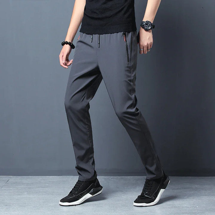 Man wearing gray casual pants and black sneakers standing against gray background