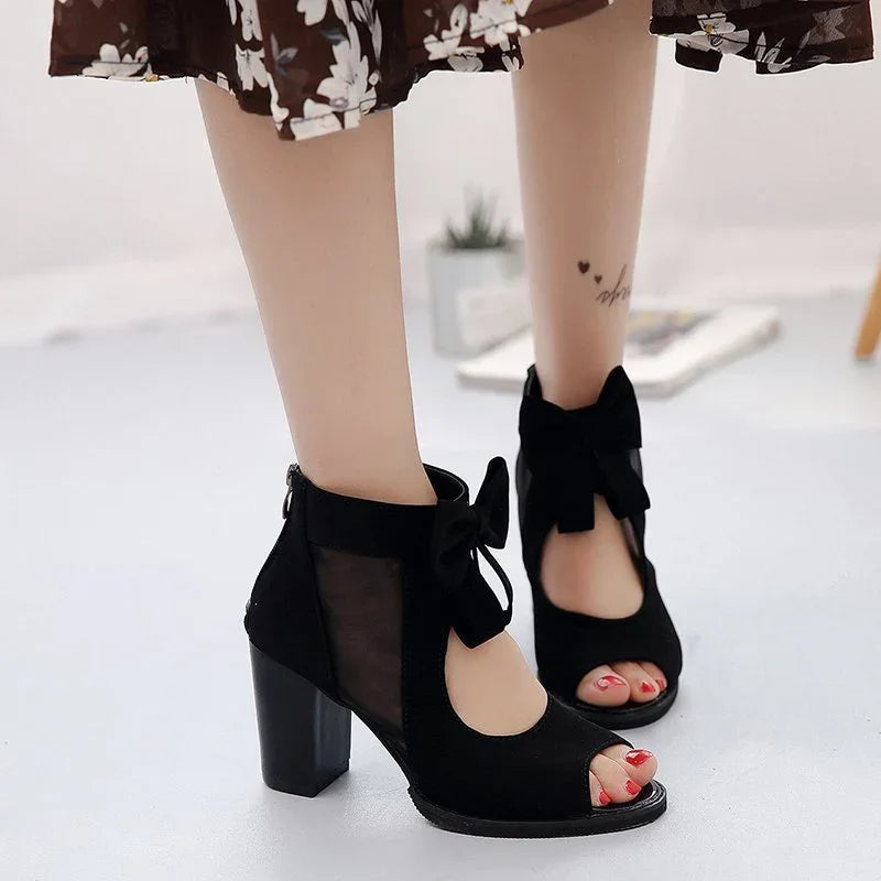 Black high-heeled ankle boots with mesh sides and bow detail, worn with a floral skirt