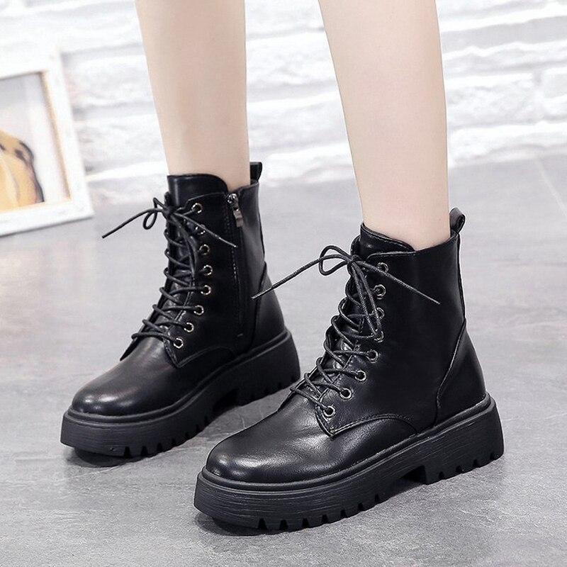 pair of black leather lace-up ankle boots with thick sole worn on feet on gray floor