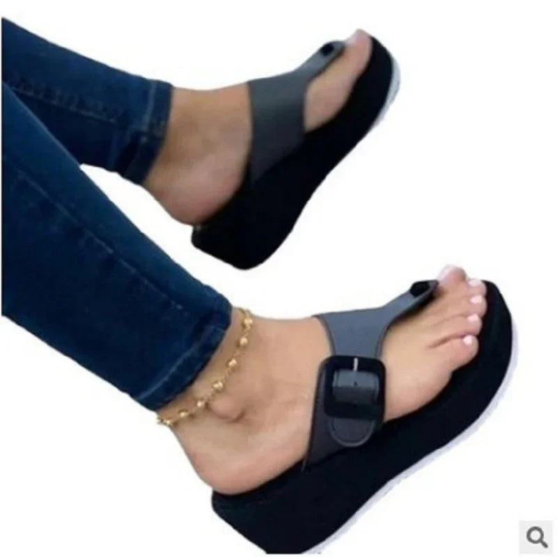 Feet wearing black platform sandals with a wide buckle strap, paired with blue jeans and gold anklet