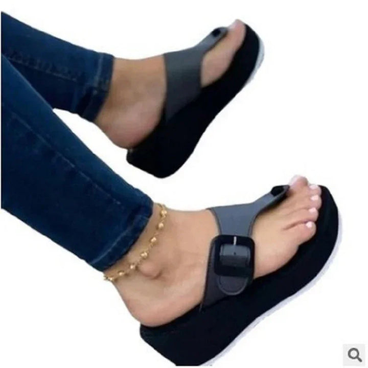 Feet wearing black platform sandals with a wide buckle strap, paired with blue jeans and gold anklet