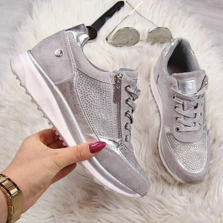 Silver glittery sneakers with side zipper and lace-up design on white fluffy surface with sunglasses and watch