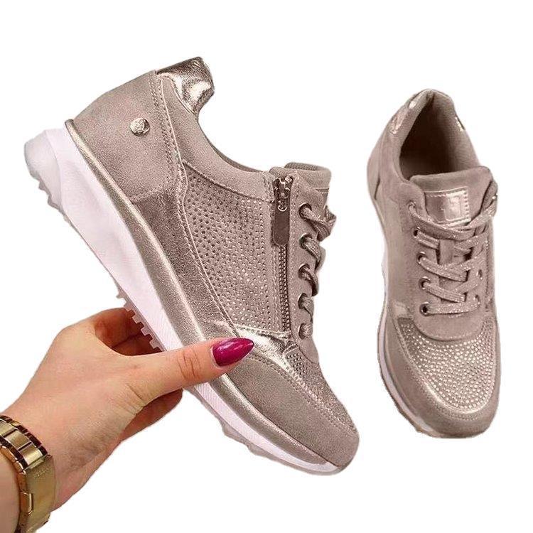Pair of stylish beige metallic sneakers with side zipper and white soles, held by hand