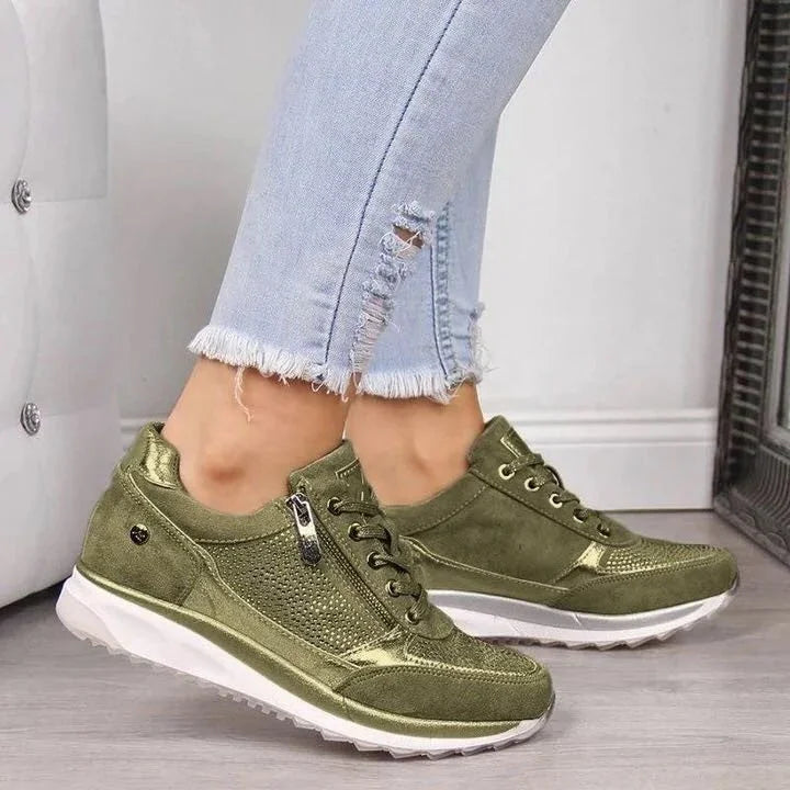 Close-up of feet wearing olive green suede sneakers with side zipper and white soles, paired with light blue frayed jeans