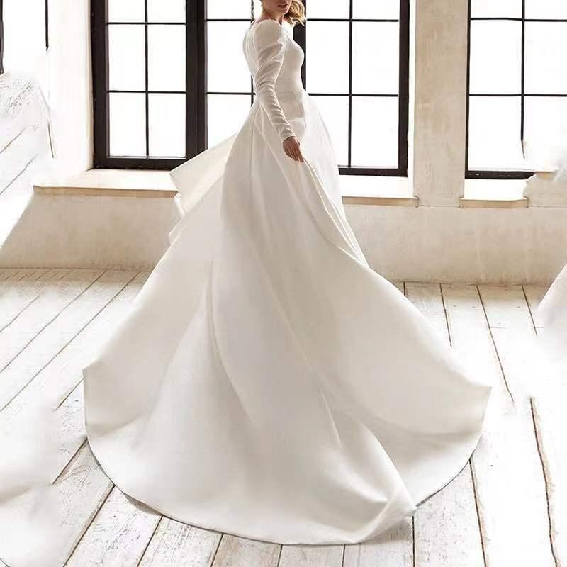 Woman in elegant long-sleeve white wedding dress twirling in bright room with large windows