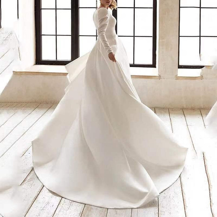 Woman in elegant long-sleeve white wedding dress twirling in bright room with large windows