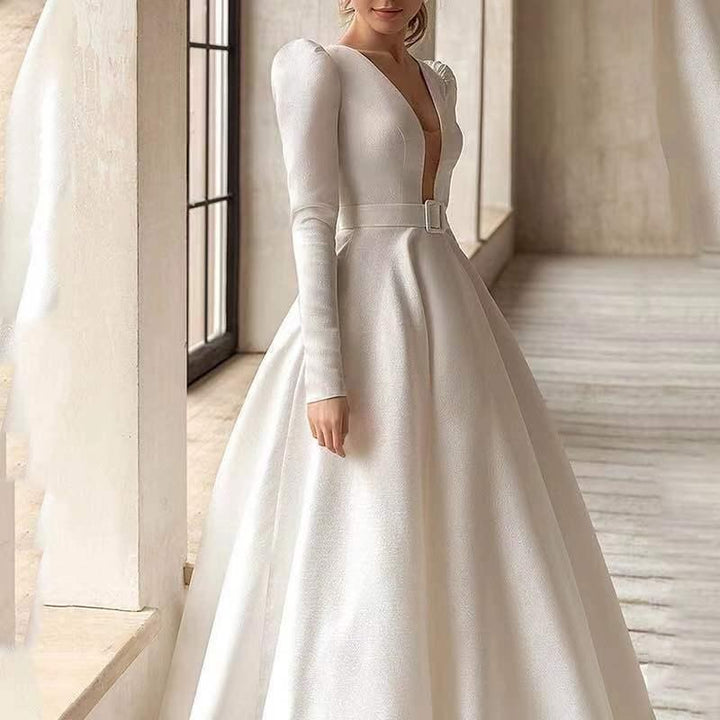 Elegant white wedding dress with deep V-neck, long puff sleeves, belted waist, and full skirt in bright room