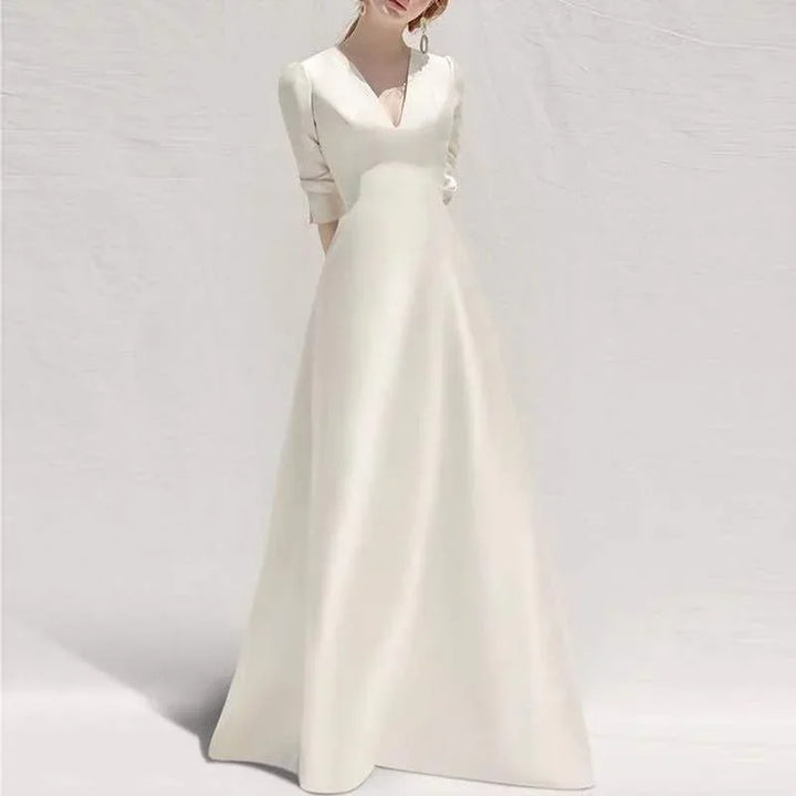 Elegant white bridal gown with V-neck and three-quarter sleeves on model against plain background