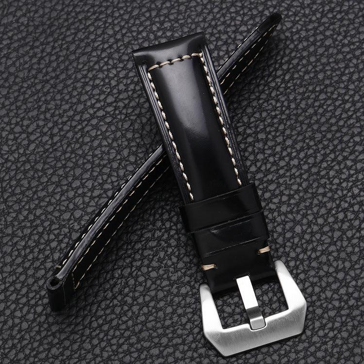 Black leather watch strap with white stitching and a silver metal buckle on textured black background