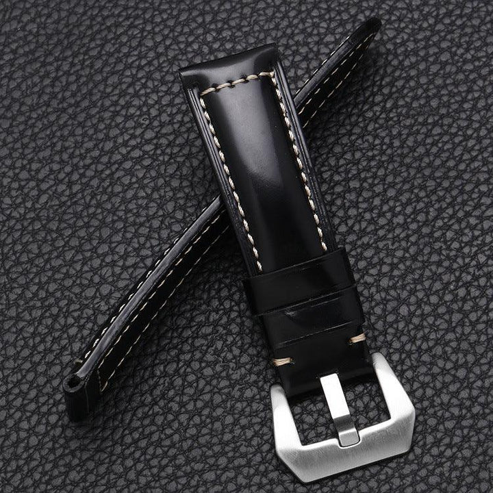 Black leather watch strap with white stitching and a silver metal buckle on textured black background