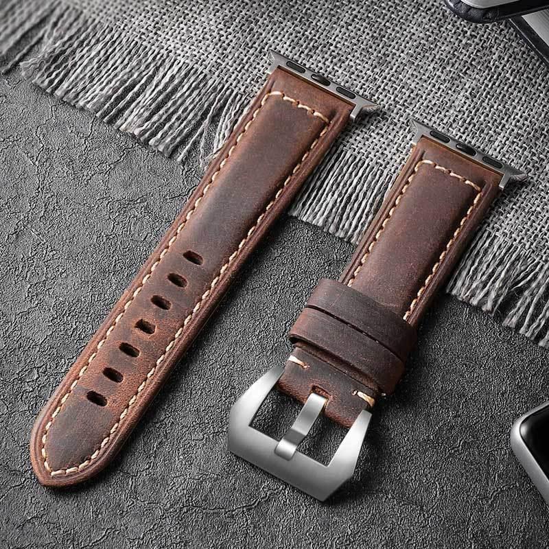 brown leather watch strap with silver buckle and stitching on dark textured surface