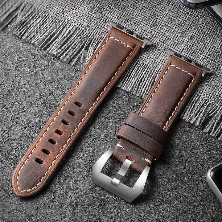 brown leather watch strap with silver buckle and stitching on dark textured surface