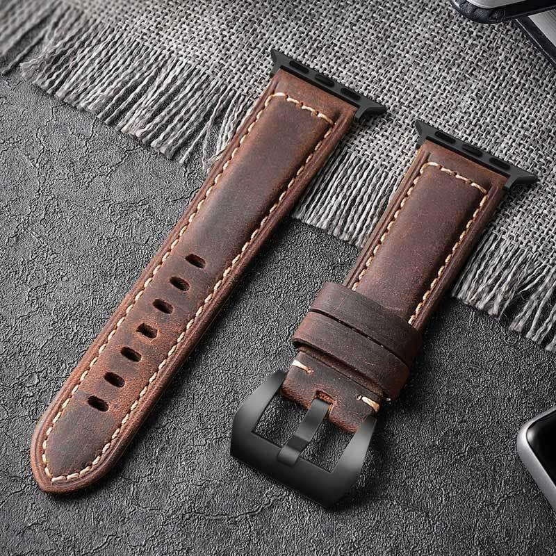 Brown leather watch strap with black buckle on textured gray surface and fringed fabric