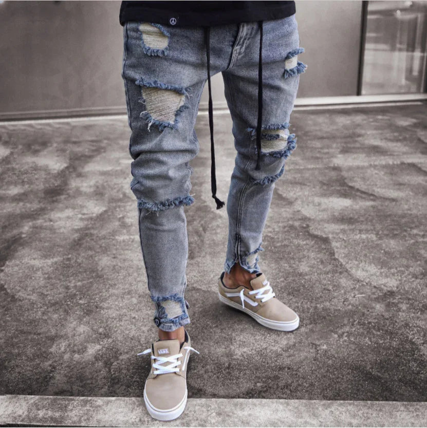 Slim fit distressed blue jeans with frayed patches worn with beige Vans sneakers on concrete floor
