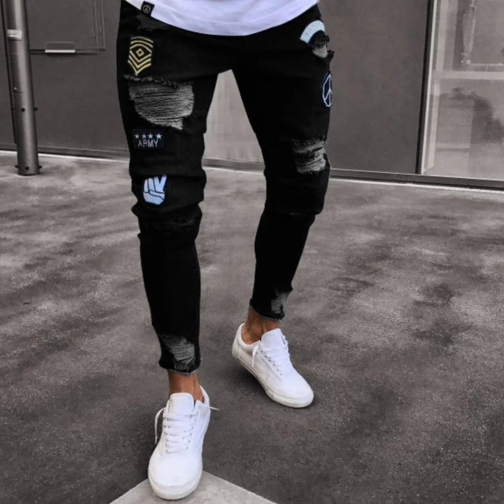 Man wearing black ripped jeans with army patches and white sneakers standing on concrete
