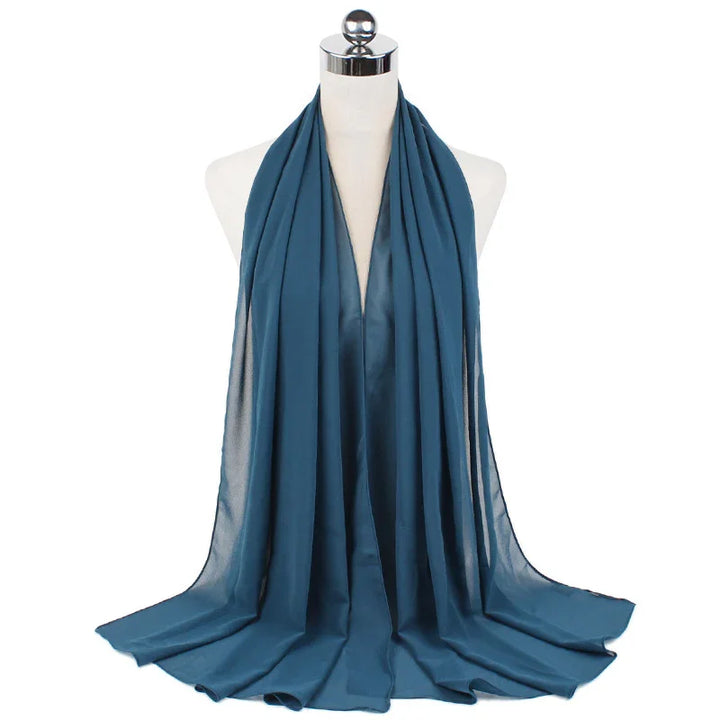 Blue chiffon scarf draped on white mannequin with silver top against white background