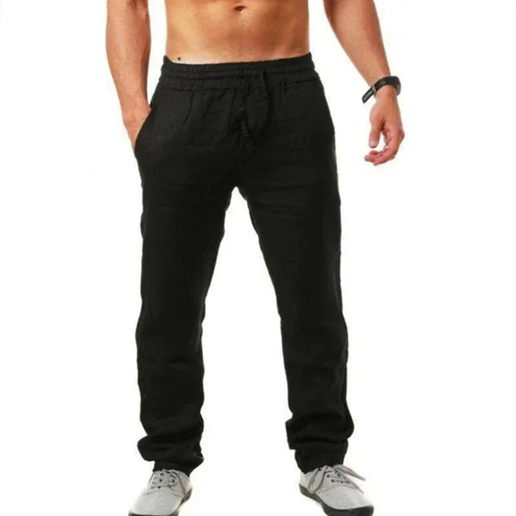 Man wearing black casual jogger pants with pockets and gray sneakers on white background