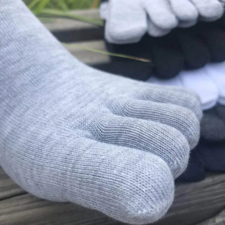 Close-up of light gray toe socks on wood surface with stacks of black, white, and gray socks in background