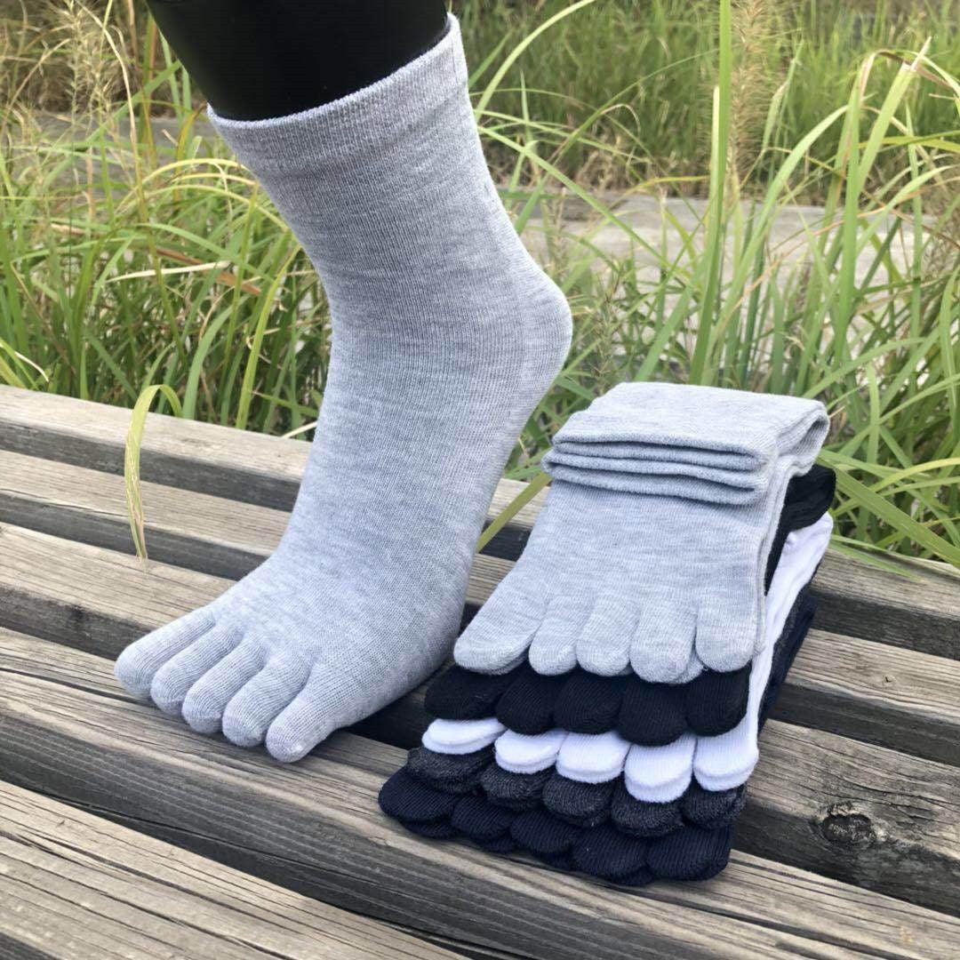 Stack of colorful toe socks with one light gray toe sock worn on foot, outdoor wooden bench