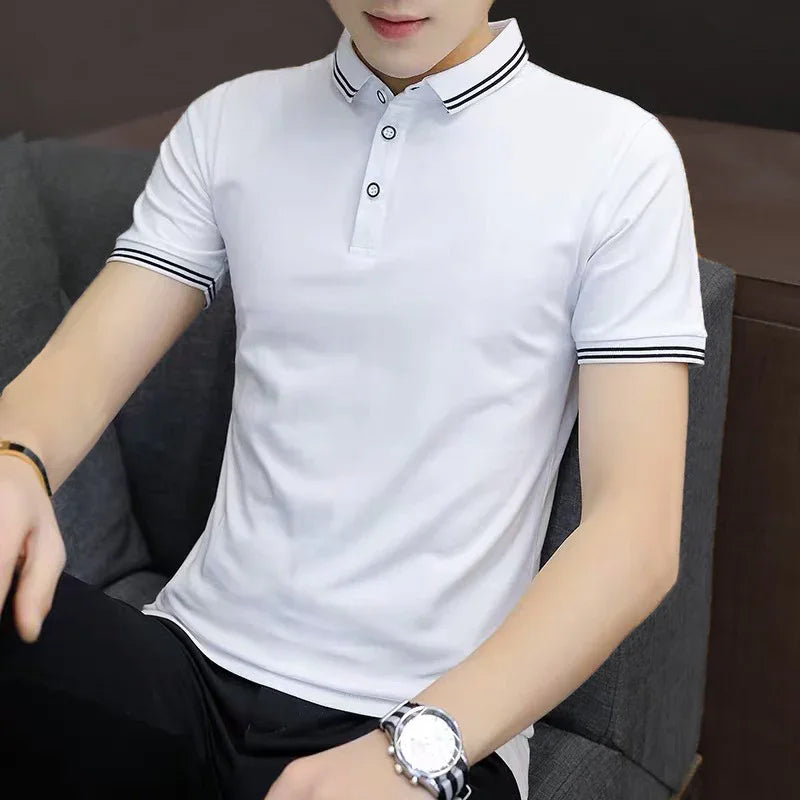 Man wearing a white short-sleeve polo shirt with black striped collar and cuffs, sitting on a gray couch