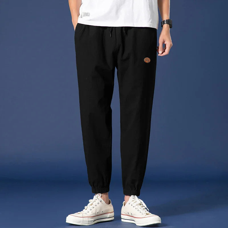 Man wearing black casual jogger pants with elastic cuffs and white sneakers on blue background