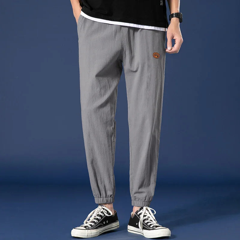 Man wearing gray casual jogger pants with elastic cuffs and black sneakers against blue background
