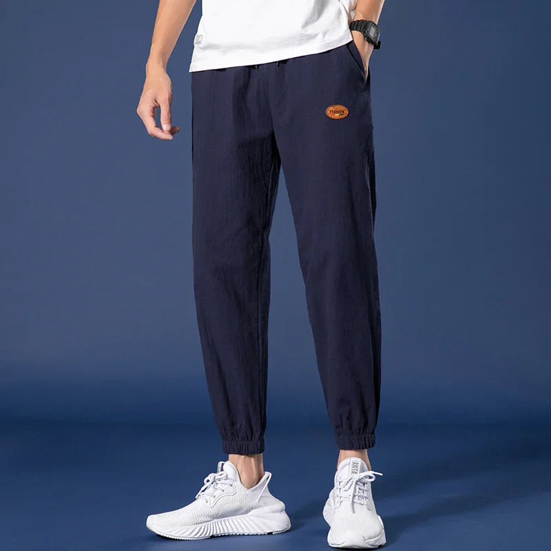 Man wearing navy blue casual jogger pants with elastic cuffs and white sneakers on blue background