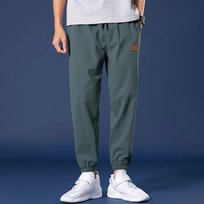 Men's casual dark green jogger pants with elastic cuffs and white sneakers on dark background