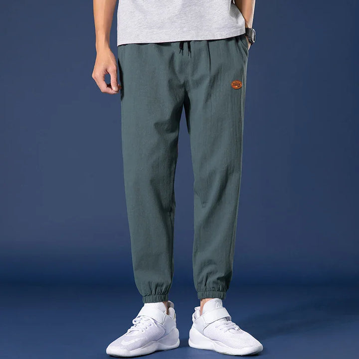 Men's casual dark green jogger pants with elastic cuffs and white sneakers on dark background