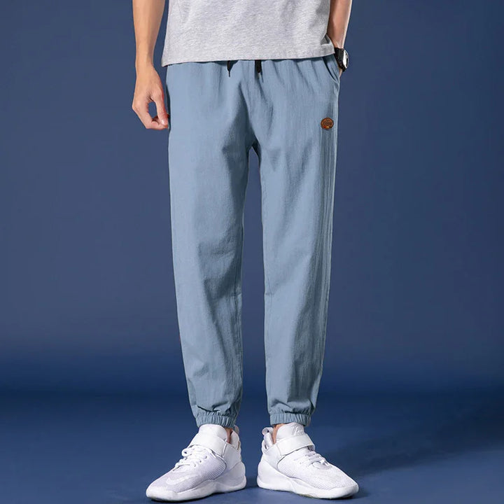 Men's casual light blue jogger pants with elastic cuffs and white sneakers on blue background
