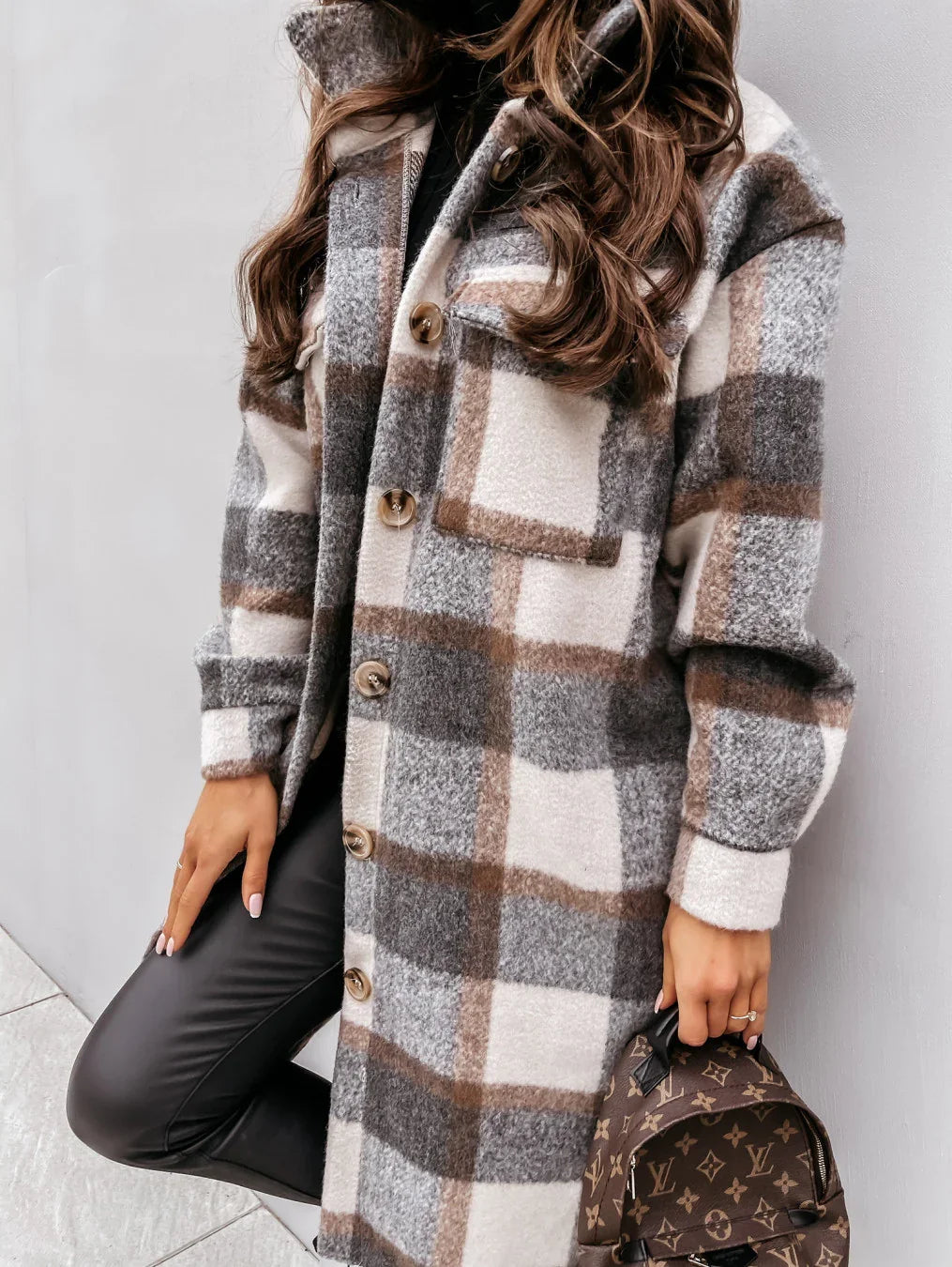 Woman wearing brown, gray, and white plaid wool coat with large buttons and holding a Louis Vuitton backpack