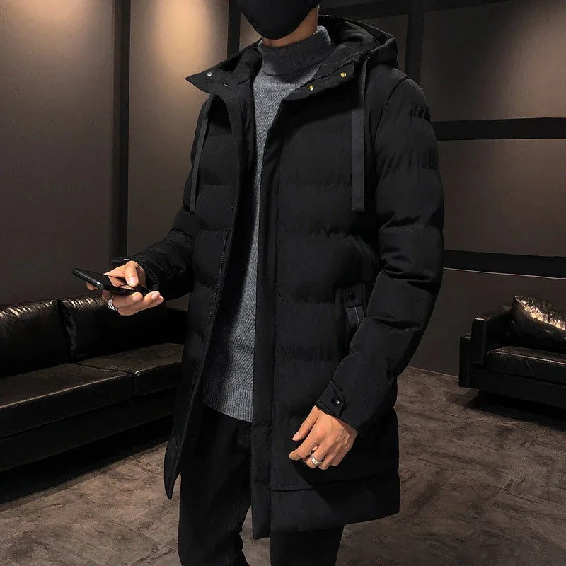 Man wearing black hooded puffer winter coat with grey turtleneck indoors holding smartphone