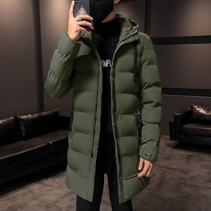 Person wearing an olive green long puffer jacket with hood and black accents indoors