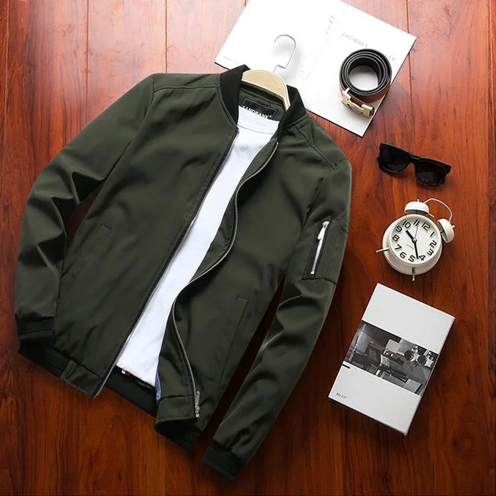 Dark green bomber jacket with white inner shirt on wooden floor with sunglasses, belt, clock, and book
