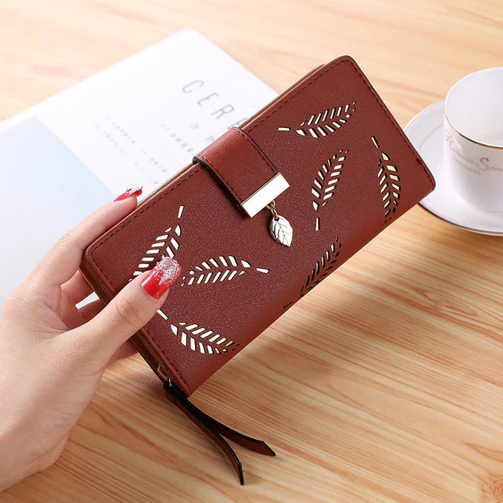 hand holding brown leather wallet with leaf cutout design and gold leaf charm on wooden table