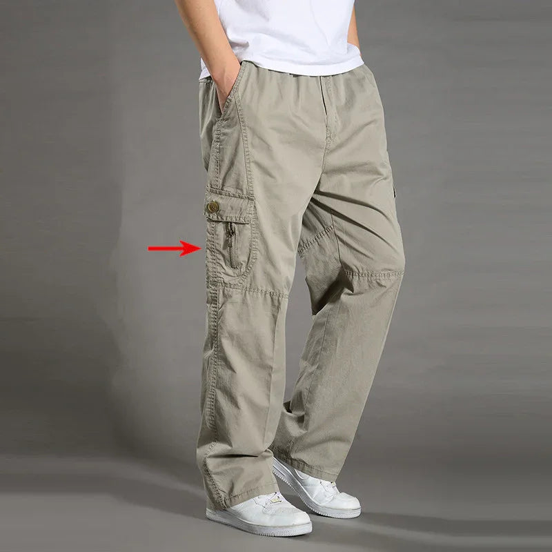 Man wearing beige cargo pants with multiple pockets and white sneakers on gray background