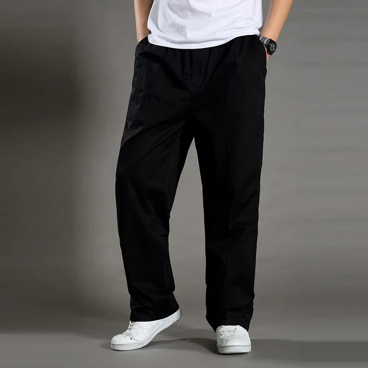 Man wearing loose black pants with white sneakers and a white t-shirt against gray background