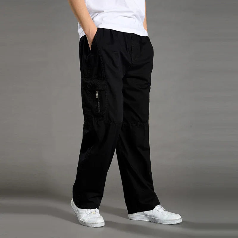 Person wearing black cargo pants with side zipper pocket and white sneakers on gray background