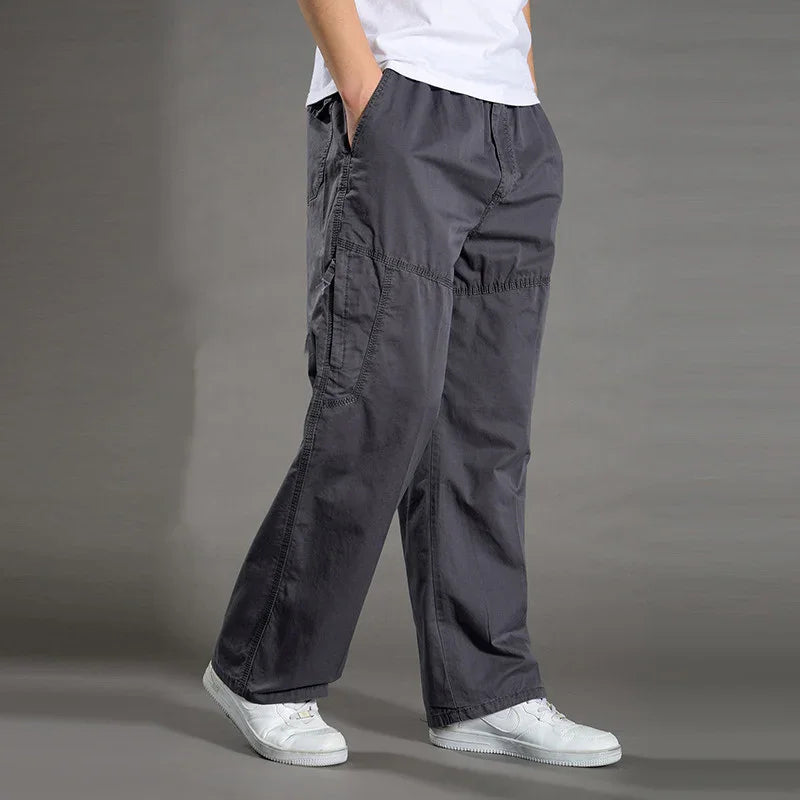 Man wearing loose dark grey cargo pants with pockets and white sneakers on grey background